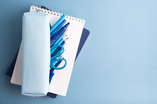 Blue stationery items including a pencil case, pens, pencils, and scissors on a light blue background, studio shot.