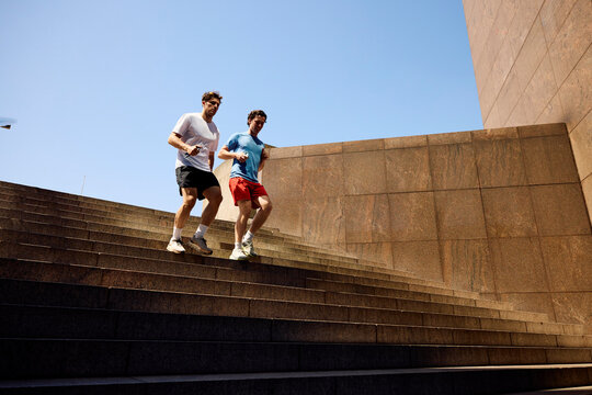 Active men run down the stairs in a sunny outdoor setting.