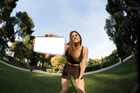 Woman holds phone while exercising in a park on sunny day