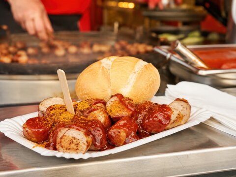 Currywurst mit w&uuml;rziger Sauce und Br&ouml;tchen am Volksfeststand &ndash; Der beliebte deutsche Imbiss wird frisch vom Grill serviert und steht f&uuml;r deftigen Genuss und Tradition.