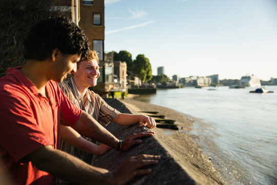 Two young men laughing by the Thames riverbank in London