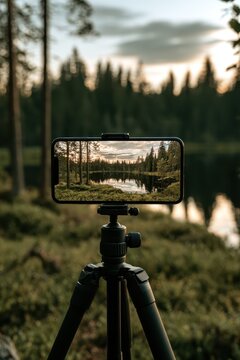Close-up of a smartphone on a compact tripod capturing a tranquil forest lake