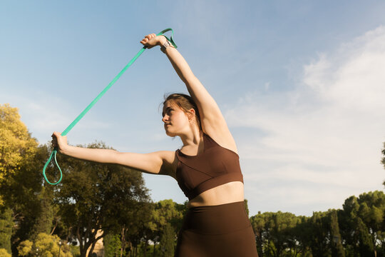 Woman uses resistance band during outdoor workout under blue sky