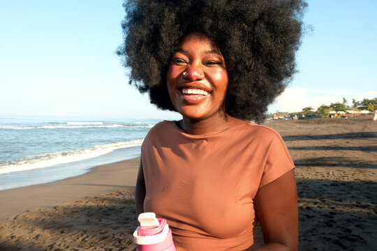 Happy woman holding a reusable water bottle at the beach