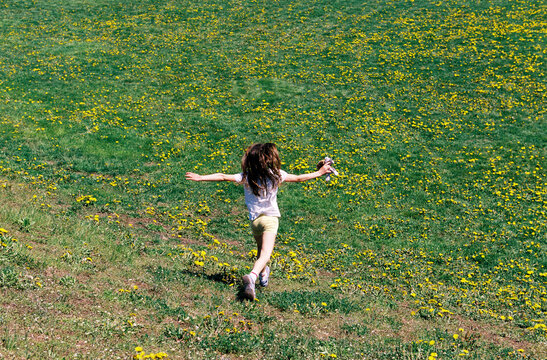 Child runs and plays outside in a grassy field of dandelion flowers