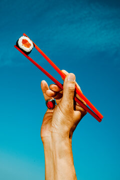 a close-up of a salmon sushi roll held between red chopsticks