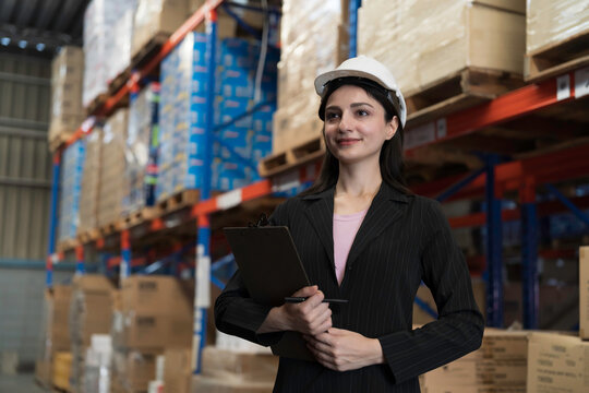 Happy smiling female warehouse worker checking items on shelf pallet at storage warehouse