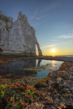 Sunlit sea arch and chalk cliffs at Etretat, Normandy, France, with rocky tide pools in the foreground