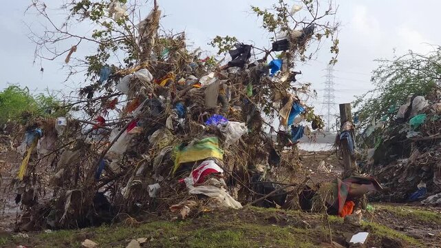 A large accumulation of plastic waste, household garbage, and debris dumped along a riverside, highlighting the growing issue of environmental pollution and poor waste management.