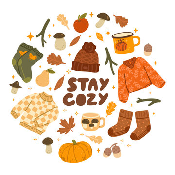 Flat vector illustration of a cozy autumn composition with sweaters, socks, hat, mugs, pumpkin, mushrooms, leaves, acorns, pear, apple and Stay Cozy lettering.
