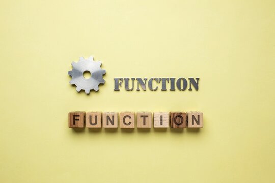 The word FUNCTION spelled out in wooden letter blocks with a gear icon against a plain yellow background symbolizing operation and mechanics