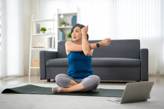 woman do excercise on a yoga mat at home, following a online workout tutorial on laptop.