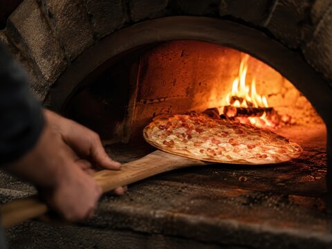 Frischer Flammkuchen wird aus dem hei&szlig;en Holzofen geholt &ndash; Offene Flammen, knuspriger Boden und handwerkliche Zubereitung zeigen rustikalen Volksfestgenuss voller Tradition.
