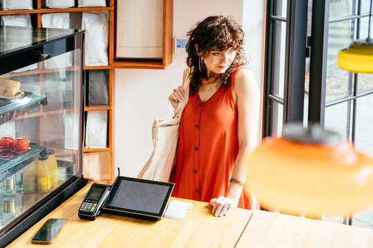 Thoughtful middle-aged woman in orange dress choosing food at modern cafe counter