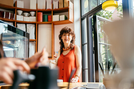 Cheerful middle-aged woman talking with barista at modern specialty coffee shop