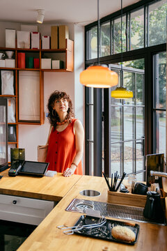 Thoughtful middle-aged woman in orange dress waiting at specialty cafe, vertical shot