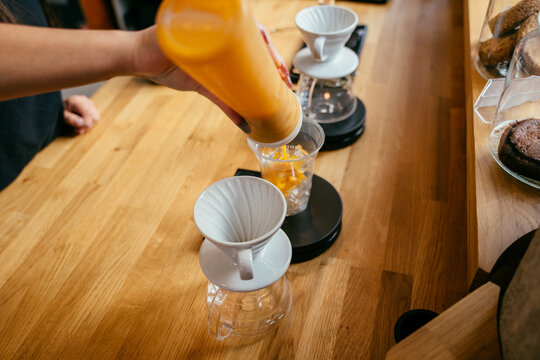 Barista pouring orange drink into glass beside pour-over coffee equipment at modern cafe