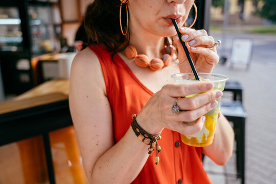Stylish middle-aged woman sipping iced matcha drink at outdoor specialty cafe, close up
