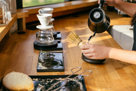 Skilled barista preparing matcha with bamboo whisk and hot water at specialty coffee shop