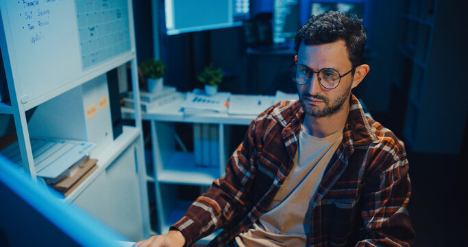Young Caucasian male programmer write code on computer in home office at late night. AI technology, cybersecurity, software developer, freelance innovation, database system, digital network concept.