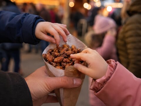 Kinderh&auml;nde greifen nach gebrannten Mandeln in einer Papiert&uuml;te &ndash; Die s&uuml;&szlig;e Volksfestszene vermittelt Teilen, Kindheit, Familienfreude und deutsche Tradition.