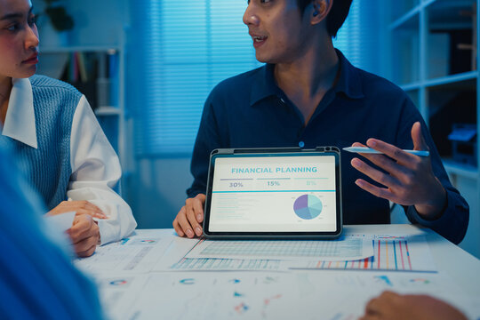 Startup Asia businesspeople meeting plan analysis statistics brainstorm and tablet point graph chart employee take note in office conference room at night. Business finance partners strategy success.