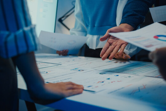 Close up Asia businesspeople meeting plan analysis statistics brainstorm and work with paperwork around table in office conference room at night. Business finance partners strategy investment success.
