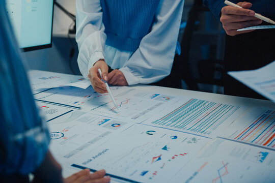 Close up Asia businesspeople meeting plan analysis statistics brainstorm and work with paperwork around table in office conference room at night. Business finance partners strategy investment success.