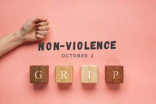 Concept of International Day of Non-Violence on October 2 with wooden blocks spelling GRIP and clenched fist on pink background