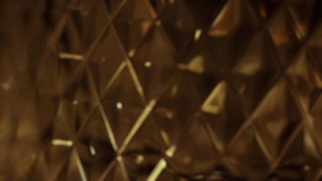 Abstract golden geometric pattern background with real light effects and subtle lens flares creates a luxurious and modern design concept. The faceted surface reflects and refracts light, producing a