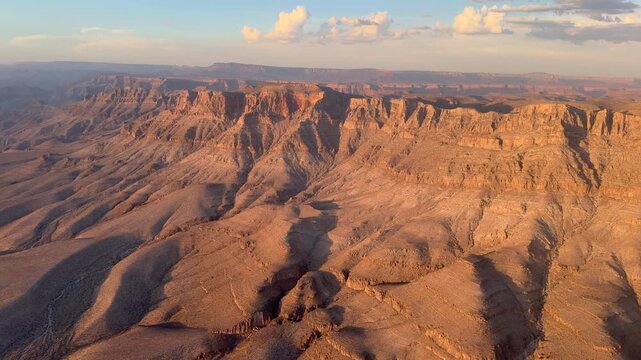 4k aerial video footage - flying along steep rock face in the Grand Canyon, located in Grand Canyon National Park, Arizona, United States, during sunset with orang illuminated mountains and valleys 