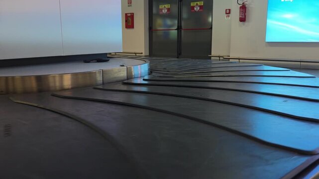 Low angle tracking shot of empty luggage carousel rotating on conveyor belt in airport terminal baggage claim area