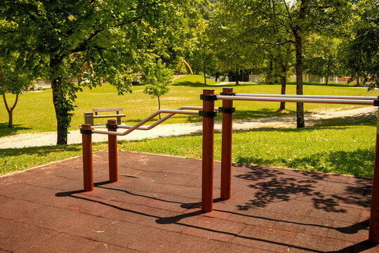 Parallel dip bars on rubber flooring at an outdoor workout park on a sunny summer day. Ideal for street workout, outdoor fitness, active lifestyle, and modern park design concepts.