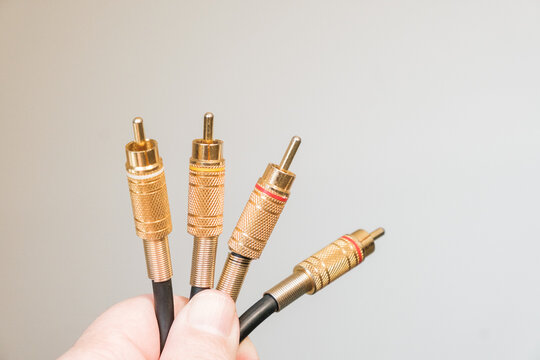 Hand holding four gold-plated RCA audio video plugs