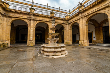 Fototapeta premium Step into centuries of history the sunlit baroque courtyard of Seville University, featuring an ornate stone fountain framed by classical arches and golden limestone colonnades. Perfect for.