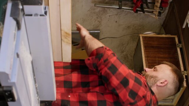 Vertical video. Professional carpentry. Lumber craft. Male joiner preparing smoothed plank for diy project in carpentry equipped with tools.
