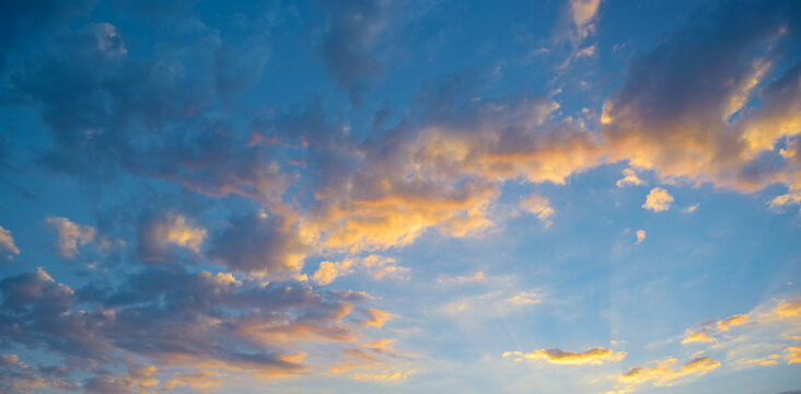 Majestic atmospheric sunset scene with glowing orange pink clouds and sun rays piercing dramatic blue sky at horizon creating tranquil mood with ample copy space