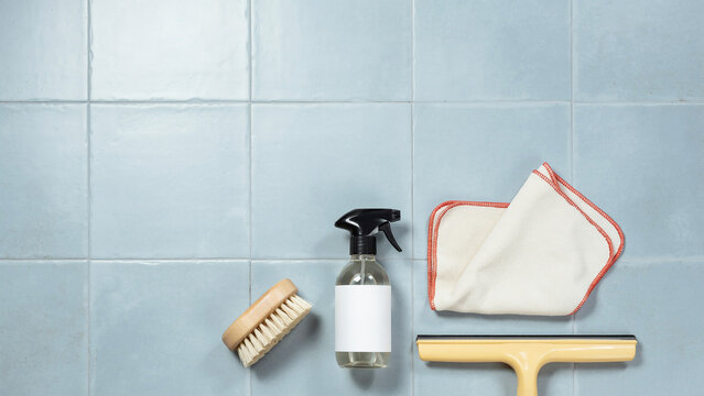 Cleaning supplies with spray bottle squeegee brush and cloth on tiled surface