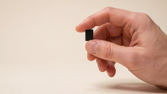 Hand holding small black microchip against plain neutral background
