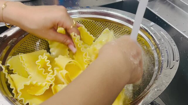 Woman separating lasagna pasta sheets in metal colander close up 16:9, Italian cooking food preparation concept
