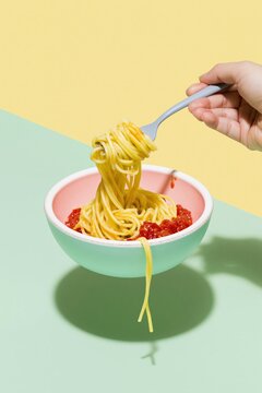 Hand twirling a nest of spaghetti with red tomato sauce in a modern mint and pink bowl, featuring a clean minimalist aesthetic for food culture and Italian cuisine concepts