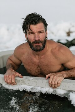 Bearded man lowering himself into a cold plunge barrel with icy water for recovery technology and wellness campaigns, featuring misty background copy space