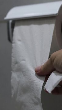 Una mano de mujer adulta agarrando papel higi&eacute;nico movi&eacute;ndolo o agarrando para realizar su limpieza cotidiana en el ba&ntilde;o. Estilo de vida. Video vertical     