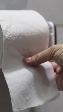 Una mano de mujer adulta agarrando papel higi&eacute;nico movi&eacute;ndolo o agarrando para realizar su limpieza cotidiana en el ba&ntilde;o. Estilo de vida. Video vertical     