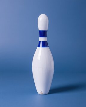 Single white bowling pin with blue stripes on a dark blue background with gloss finish and soft reflections for sports and leisure concepts
