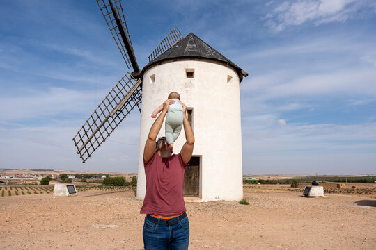 Father lifting baby in front of traditional Spanish windmill