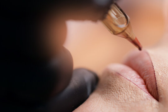 Master use tattoo machine for applying permanent makeup of red on lips woman with sunlight