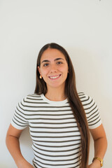 Fototapeta premium Young woman with brown hair smiling confidently while looking at the camera, wearing a striped shirt and expressing genuine happiness
