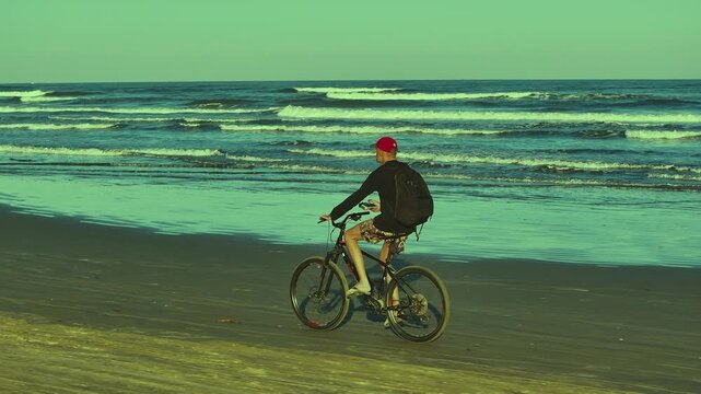 Cyclist riding along the beach with ocean waves in the background. Healthy outdoor fitness and active lifestyle by the sea. 4K video.