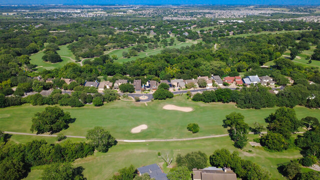 Sprawling green fairways in Onion Creek line homes parallel to Pebble Beach Drive in suburbs Austin. Manicured hazards blend with residential rooftops along tree lined streets